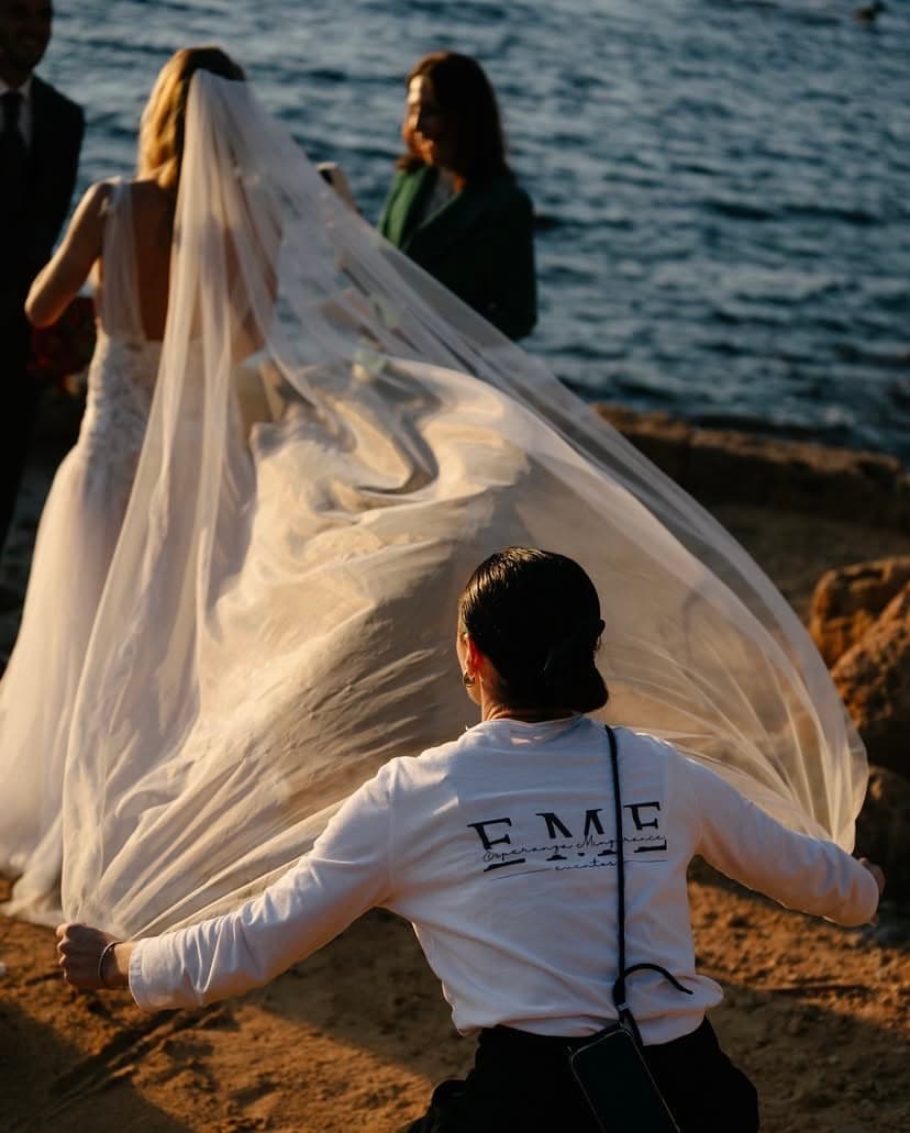 Wedding planner de EME Eventos colocando el velo de la novia en una ceremonia junto al mar al atardecer